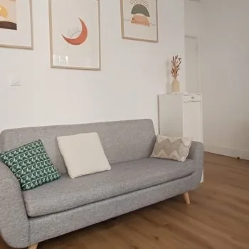 Salle du cabinet avec un canapé gris, des coussins et des affiches aux tons doux